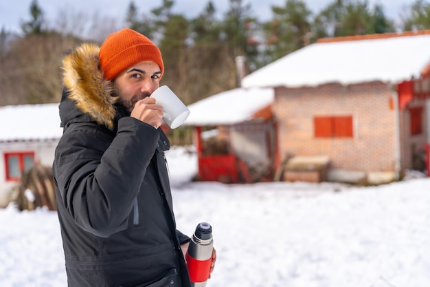 Hombre bebiendo café de un termo caliente en invierno en la nieve junto a una cabaña Artikutza Gipuzkoa