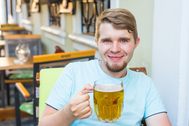 Hombre bebiendo cerveza. Apuesto joven bebiendo cerveza mientras está sentado en el bar al aire libre