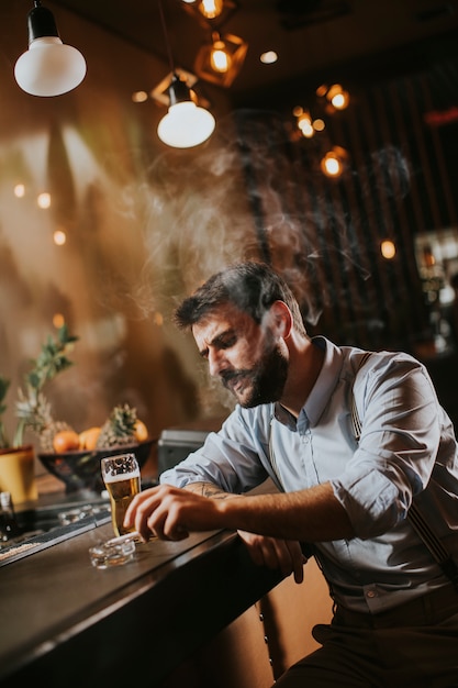 Hombre bebiendo cerveza y fumando cigarrillo en pub