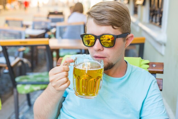 Hombre bebiendo cerveza. Hombre guapo joven inconformista bebiendo cerveza mientras está sentado en el bar al aire libre