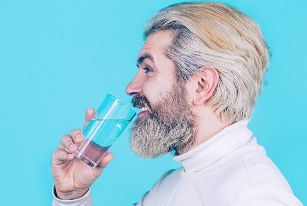 Hombre bebiendo de un vaso de agua. Agua potable de hombre barbudo. Hombre de barba feliz bebiendo agua. Concepto de salud, estilo de vida, de cerca. Varón sonriente sosteniendo vidrio transparente en su mano.