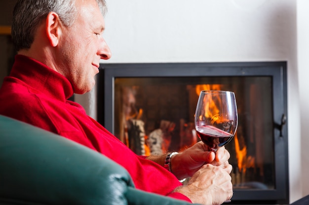 Hombre bebiendo vino tinto en la chimenea