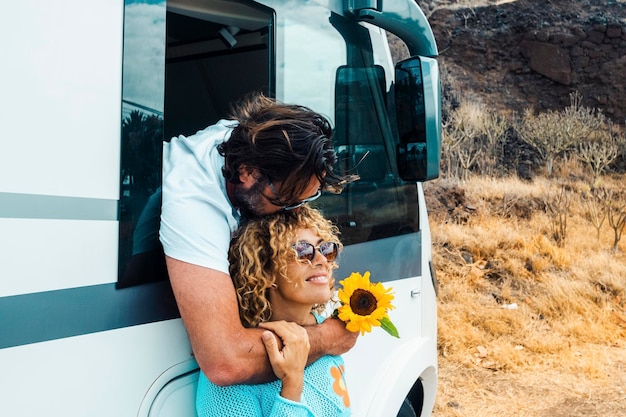 El hombre besa a la mujer y ambos disfrutan del estilo de vida de los viajes La pareja feliz se abraza y sonríe en una relación contra una autocaravana moderna Vacaciones alternativas en la carretera y libertad fuera de la red