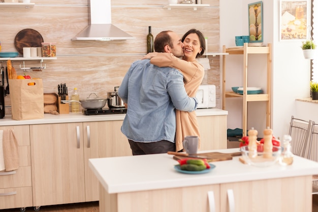 Hombre besando a la esposa en la cocina durante el baile romántico en la cocina. Amor de esposa y esposo, romance, momento tierno, diversión y felicidad en el hogar, música de unión alegre y sonrisa