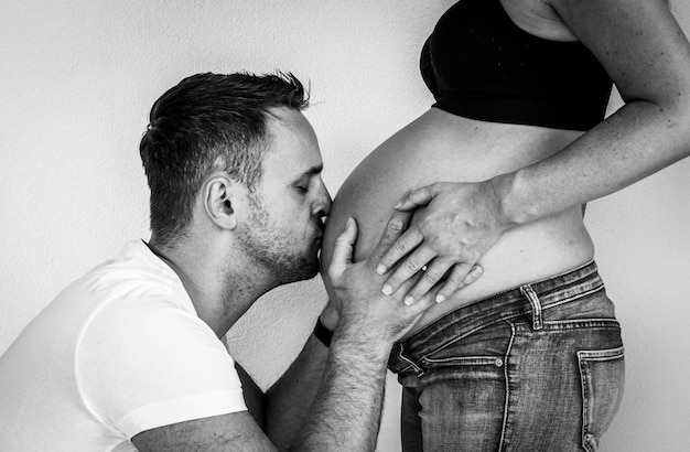 Foto hombre besando a hombre mujer embarazada abdomen contra la pared