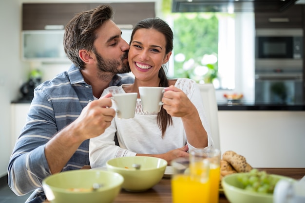 Hombre besándose en las mejillas de la mujer mientras desayuna