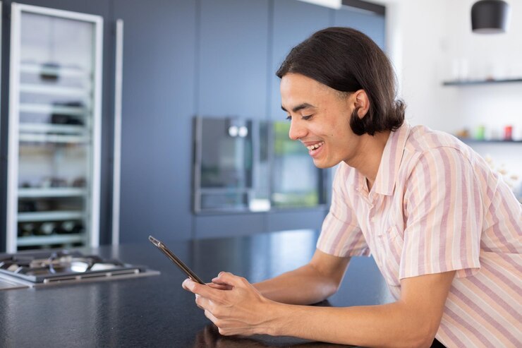Foto hombre bi-racial feliz usando tableta en la cocina, pasando tiempo de calidad en casa solo, vida doméstica y concepto de estilo de vida.