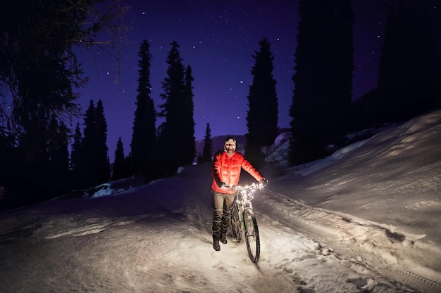 Hombre con bicicleta en el bosque de invierno por la noche