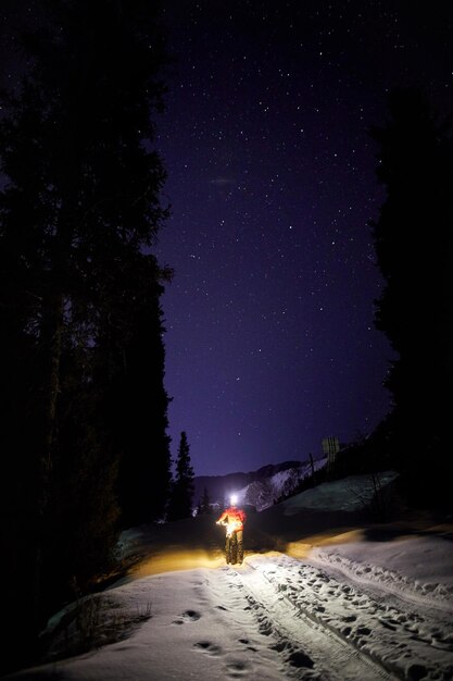 Hombre con bicicleta en el bosque de invierno por la noche