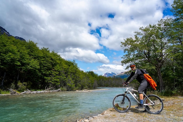 Foto hombre en bicicleta en el bosque junto al río con montañas al fondo