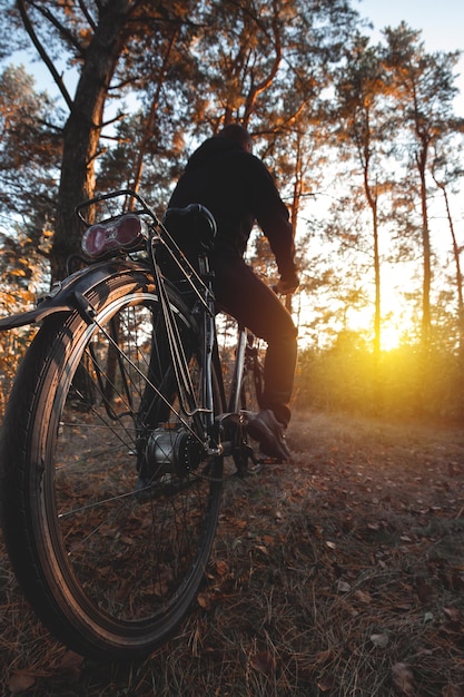 Hombre en bicicleta en el bosque de otoño por la noche al atardecer