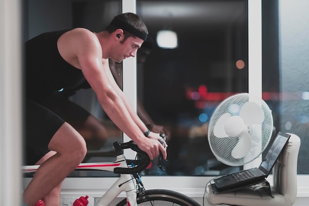 Foto hombre en bicicleta en el entrenador de la máquina está haciendo ejercicio en la casa por la noche jugando al juego de carreras de bicicletas en línea