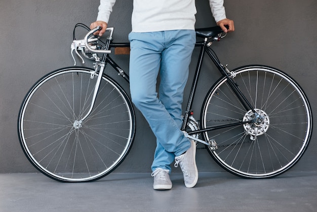 Hombre con bicicleta. Primer plano del hombre apoyado en su bicicleta mientras está de pie contra el fondo gris