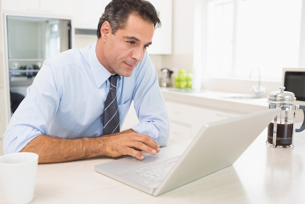 Hombre bien vestido concentrado que usa la computadora portátil en cocina