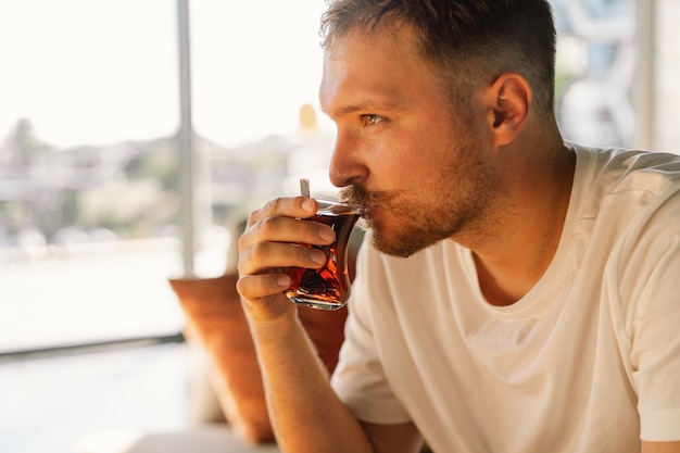 Un hombre con bigote bebe y disfruta de un té caliente tradicional turco en el vestíbulo de un hotel turco