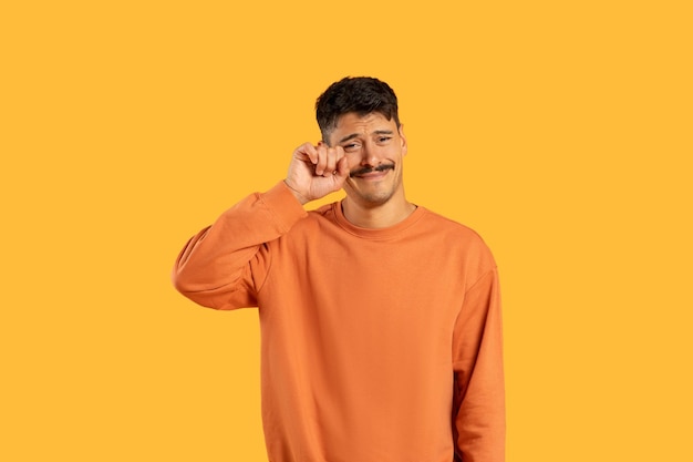 Hombre con bigote limpiando lágrimas sobre un fondo amarillo