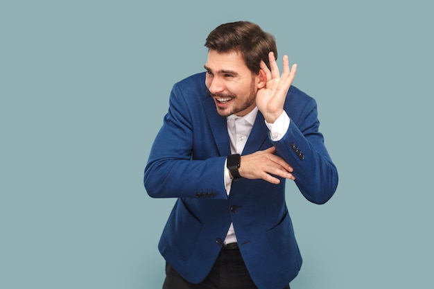 Hombre con bigote de pie con el ceño fruncido y la mano cerca de la oreja tratando de escuchar una conversación silenciosa