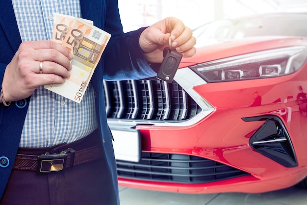 Hombre con billete de euro para comprar o alquilar un coche nuevo en una sala de exposición