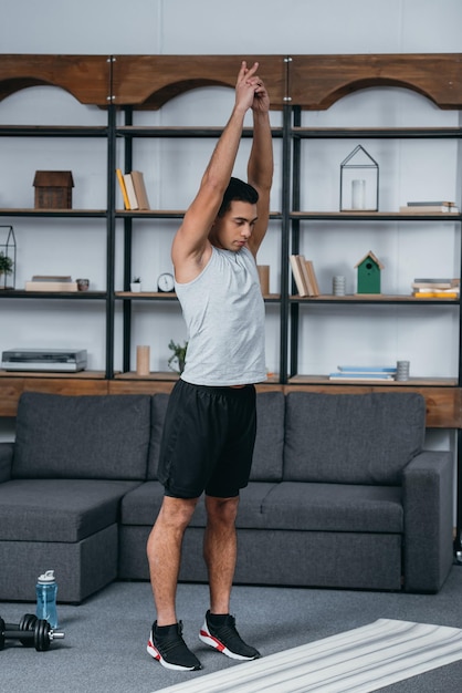 Hombre birracial guapo parado cerca de la alfombra de fitness y haciendo ejercicio