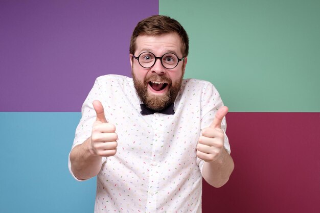 Un hombre bizarro con barba y gafas redondas hace un gesto de aprobación con las manos hacia arriba y con alegría