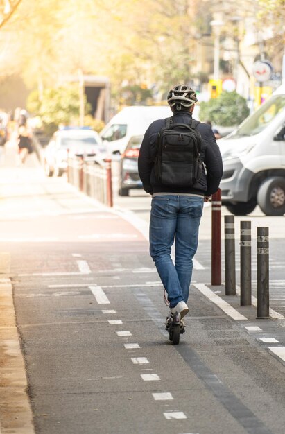 Hombre blanco por detrás con mochila y casco de bicicleta en un scooter eléctrico en un carril bici