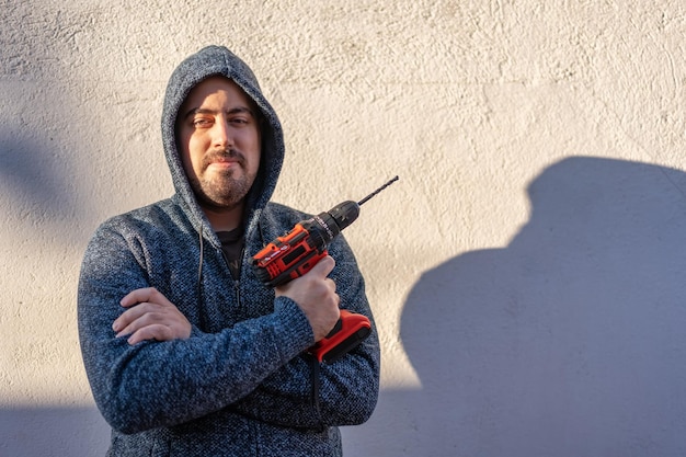 Hombre blanco mirando a la cámara con un taladro eléctrico de baterías sin cables para hacer bricolaje