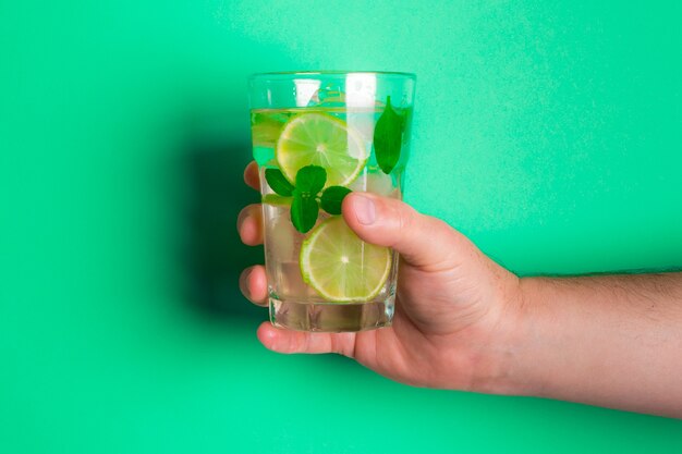 Hombre blanco sosteniendo un vaso de limonada fresca con trozos de limón y albahaca en el verde