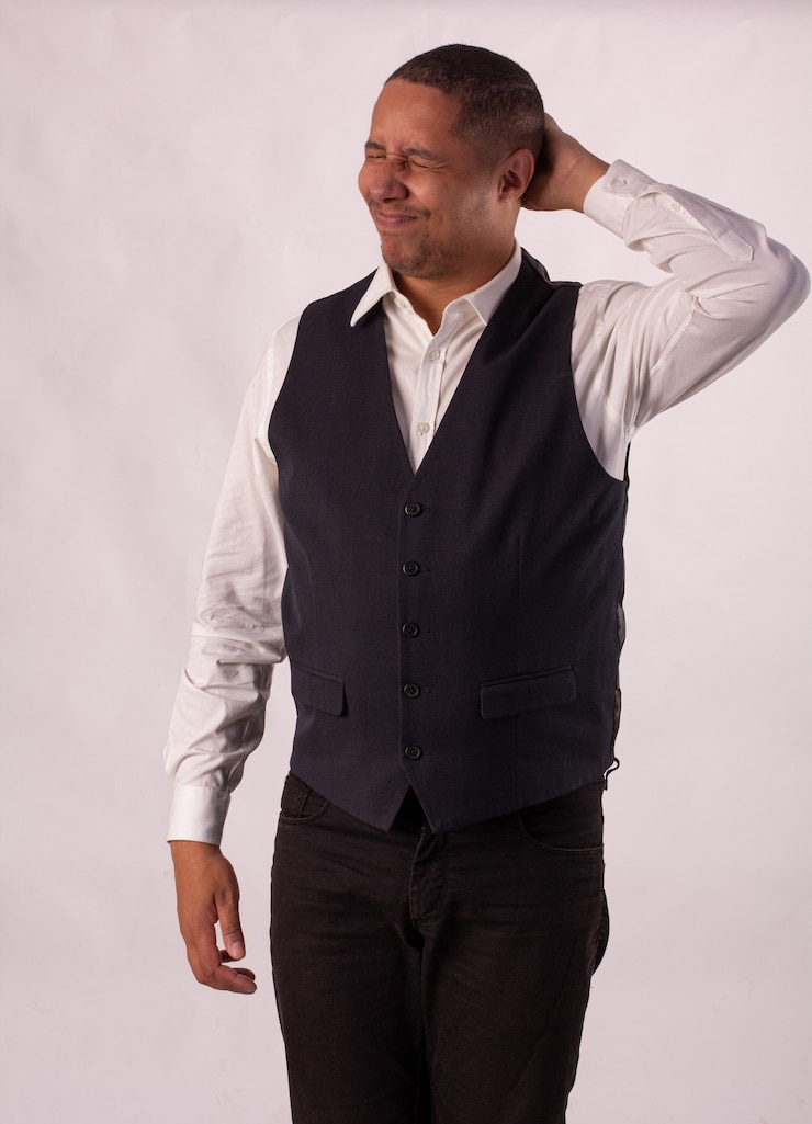 Foto hombre con blazer negro, camisa blanca y pantalón negro sobre un fondo blanco haciendo expresiones corporales.