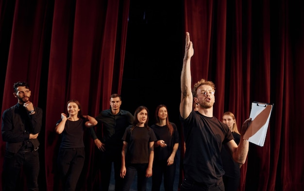 Hombre con bloc de notas practica su papel Grupo de actores con ropa de color oscuro en el ensayo en el teatro