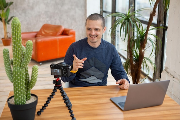 Hombre blogger con cámara y laptop filmando video para blog o para cursos en línea.