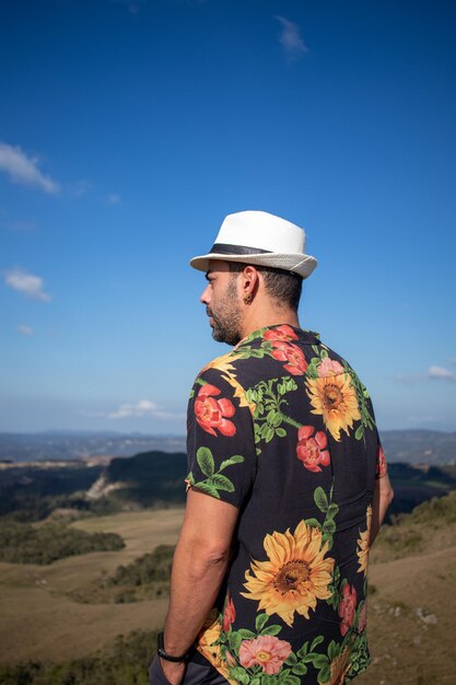 Hombre con blusa de flores y sombrero blanco en la cabeza admirando el paisaje mirando hacia un lado