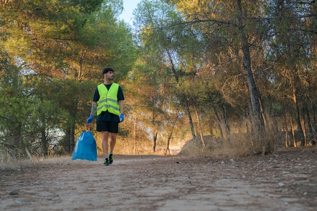 Hombre con una bolsa de basura llena de plásticos en un bosque