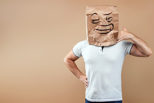 Un hombre con una bolsa de papel en la cabeza, en la que está pintada una cara malvada, finge estar hablando por teléfono. Aislado sobre fondo amarillo, fácil de recortar para usar en cualquier lugar, copie el espacio.