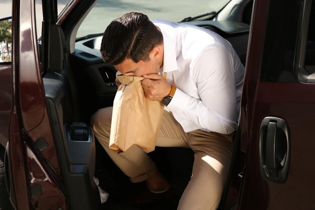 Hombre con bolsa de papel que sufre de náuseas en el coche