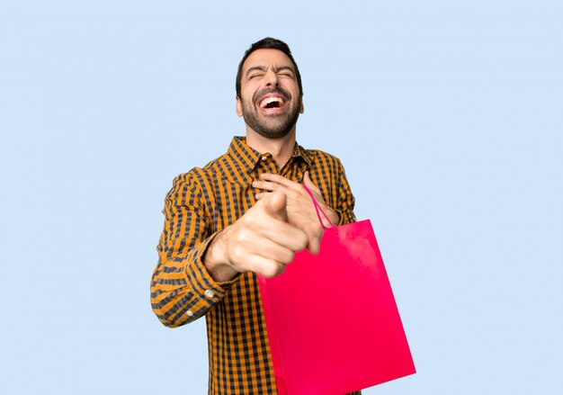 Foto hombre con bolsas de compra apuntando con el dedo a alguien y riendo mucho