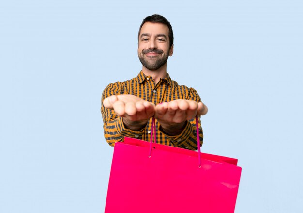 Hombre con bolsas de compra con copyspace imaginario en la palma para insertar un anuncio sobre fondo azul aislado