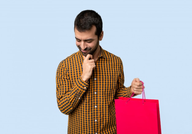 Hombre con bolsas de compras mirando hacia abajo con la mano en la barbilla sobre fondo azul aislado