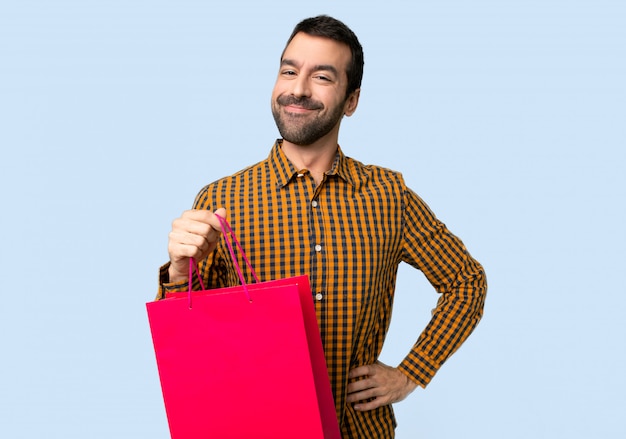 Hombre con los bolsos de compras que presentan con los brazos en la cadera y que sonríen en fondo azul aislado