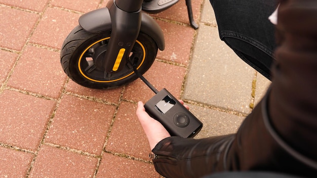 Un hombre bombea aire a la rueda de un scooter eléctrico mediante un dispositivo especial. Foto exterior. Un neumático pinchado mientras conduce.