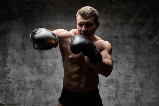 Hombre bombeado muscular boxeando en guantes sobre un fondo negro. Cuerpo atlético sexy