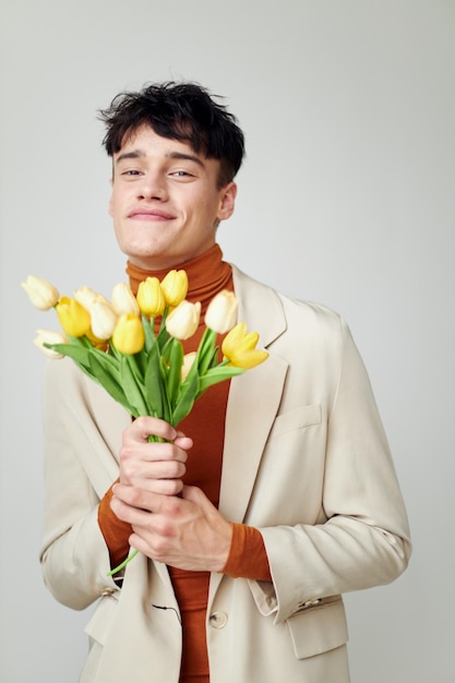 Hombre bonito en chaqueta blanca con un ramo de flores amarillas estudio de modelo de estilo elegante