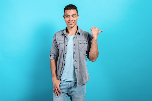 Foto hombre bonito sonriendo y apuntando hacia atrás de pie