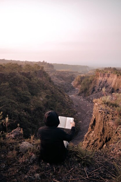 Foto el hombre en el borde del acantilado se estaba relajando y leyendo un libro kaliadem yogyakarta