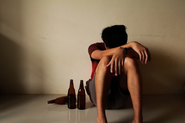 Hombre borracho con botella de cerveza tiene estrés en la vida y está sentado solo en una habitación vacía, triste, solitario, escuela, adolescencia, violencia en el hogar, problemas de amor no deseados, solo, familia