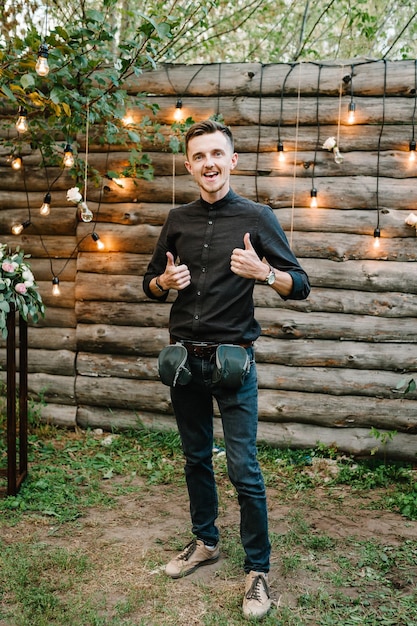 Hombre en el bosque mágico de la tarde decorado con guirnaldas de luces Amigo en la ceremonia con linternas y lámparas decoradas con flores Novio en el fondo de las luces de las bombillas