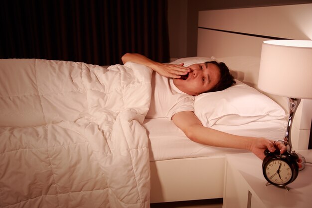 Hombre bostezando siendo despertado por un reloj despertador en su habitación por la mañana