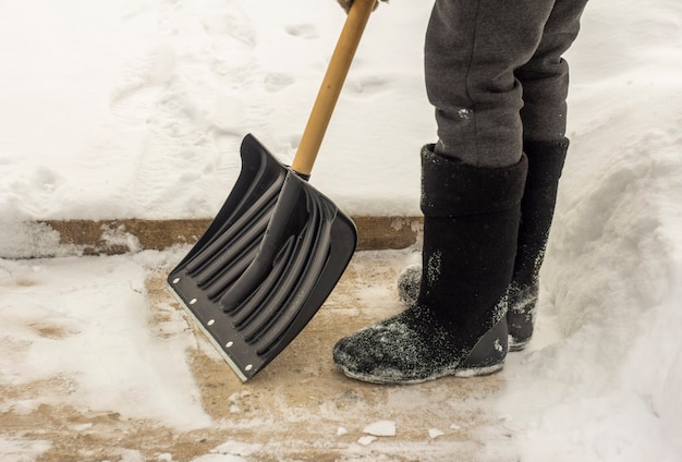 Un hombre con botas de fieltro, con una pala en la mano, quita la nieve de la acera después de una nevada.