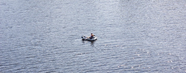 Un hombre en un bote de goma inflable con remos flota en la vista del río desde lejos