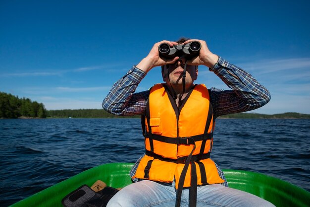 El hombre en el bote mira en los binoculares