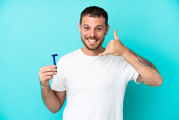 Hombre brasileño afeitándose la barba aislado sobre fondo azul haciendo gesto de teléfono. Llámame señal